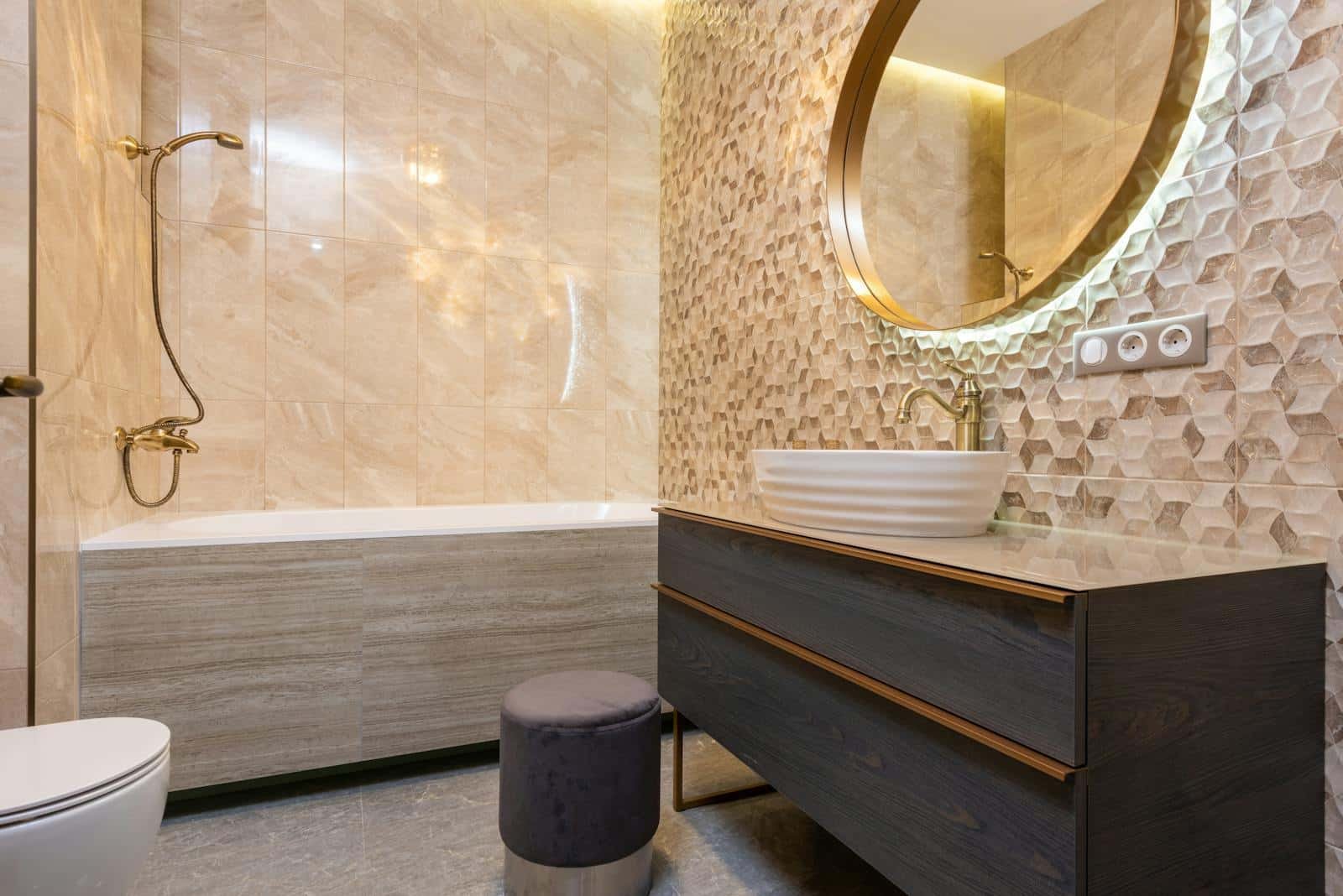 Interior of light bathroom with sink with faucet on cabinet under mirror near pouf in front of toilet next to bathtub with shower